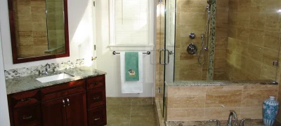 A clean and functional bathroom showcasing a spacious walk-in shower with a rainfall showerhead and a single-sink vanity with drawers for storage. The vanity has a sleek countertop and a rectangular mirror above it.