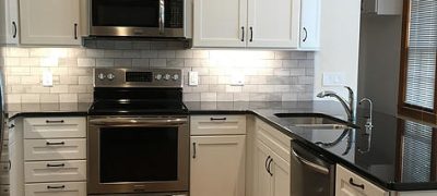 A modern kitchen featuring a minimalist design with sleek stainless steel appliances, crisp white cabinets, and contrasting black countertops. The kitchen appears clean and organized, with ample counter space for food preparation and a sink with a faucet visible in the frame.